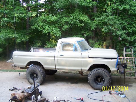 1979 Ford F-150 - A tan 1979 Ford F-150 pickup truck is parked outside with large off-road tires and blue tape around the windows.