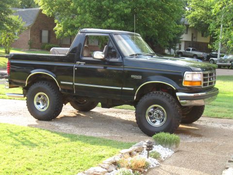 1994 Ford Bronco - This black 1994 Ford Bronco features a lifted suspension and chrome wheels, parked on a driveway.
