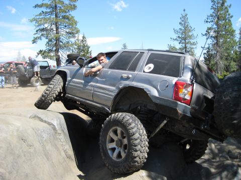 1999 Jeep Grand Cherokee - A modified Jeep Grand Cherokee navigates a challenging off-road obstacle, with another vehicle in the background.