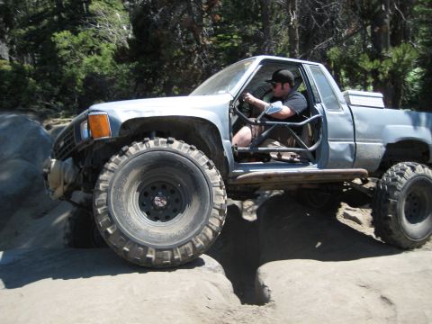 1999 Jeep Grand Cherokee - A driver maneuvers a modified pickup truck over a challenging rocky obstacle.