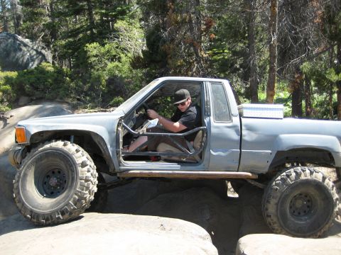 1999 Jeep Grand Cherokee - Driver in a modified pickup truck with custom roll cage and off-road tires on a trail.