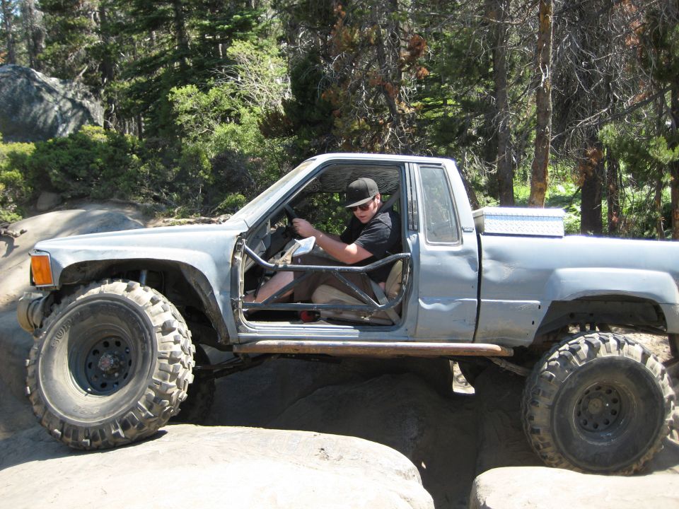 Modified pickup truck with roll cage and large off-road tires navigating rocky terrain