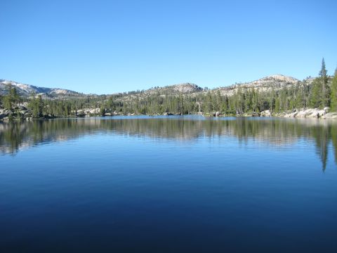 1999 Jeep Grand Cherokee - A vast blue lake is surrounded by pine trees and rocky hills under a bright, cloudless sky.