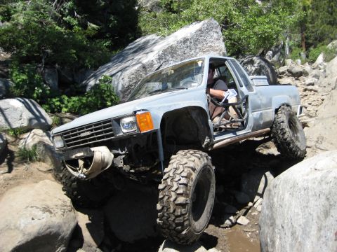 1999 Jeep Grand Cherokee - Pickup truck modified for off-roading climbs over large rocks on a trail.