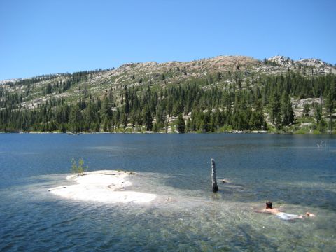 1999 Jeep Grand Cherokee - A person enjoys a swim in a calm lake surrounded by trees and a rocky mountain under a clear blue sky.