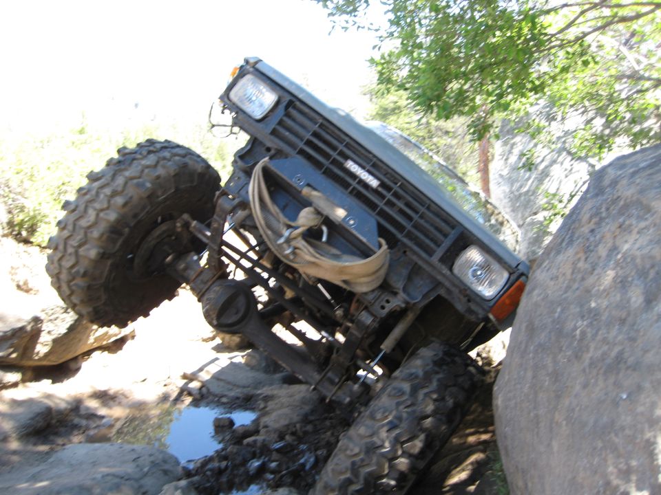 Dark gray Toyota off-road vehicle tilted on rocks with large tires and a winch