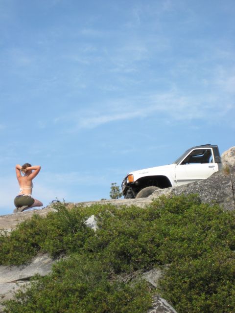 1999 Jeep Grand Cherokee - A person kneels on a rocky outcrop with a white SUV parked nearby under a clear blue sky.