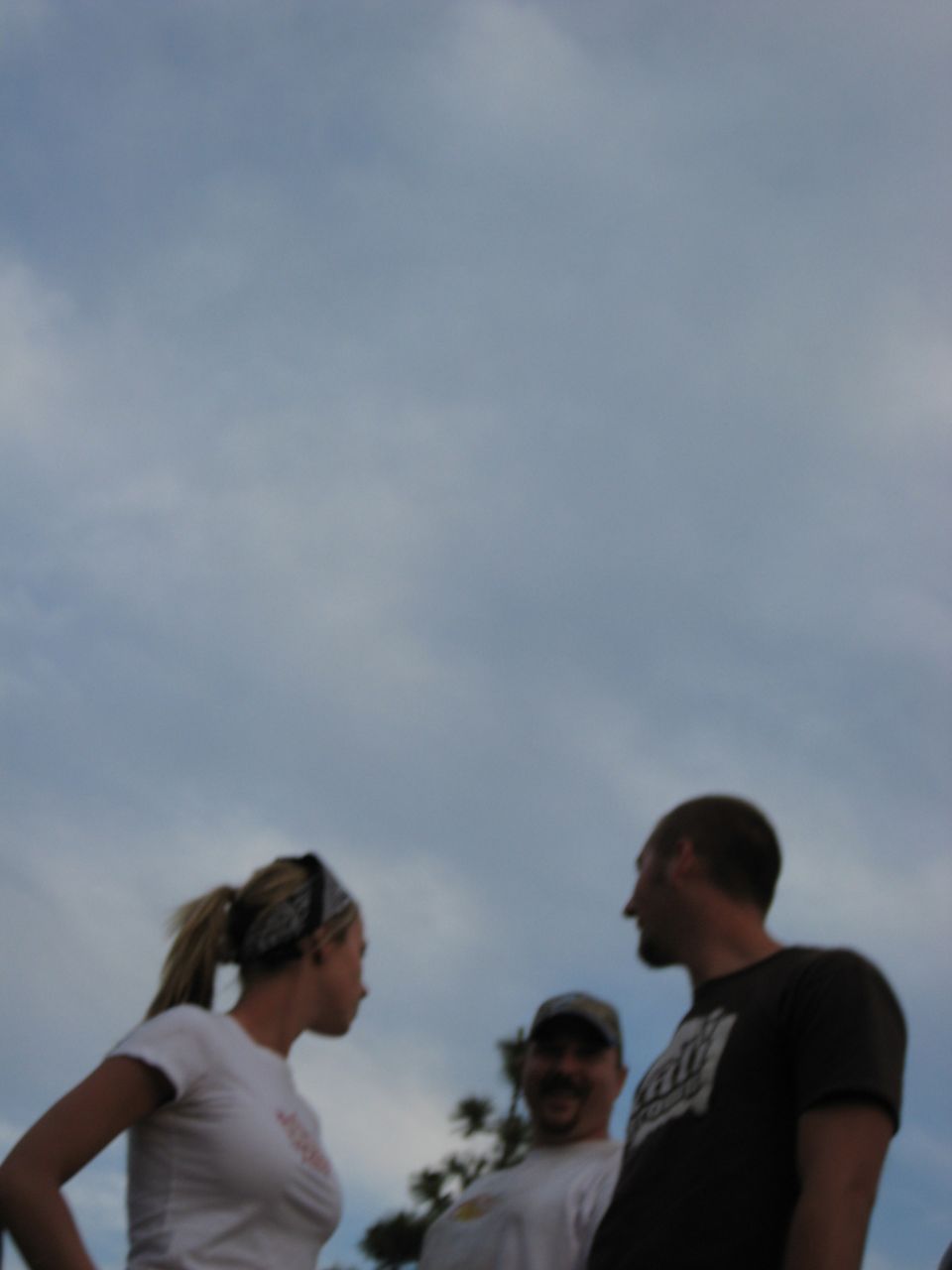 Three people converse under a cloudy sky; a watermark reads SUPERMOTORS
