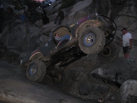 1999 Jeep Grand Cherokee - An off-road vehicle navigates a rocky incline, with spectators watching.