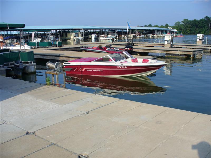 Red and white speed boat docked at a marina with covered slips in the background