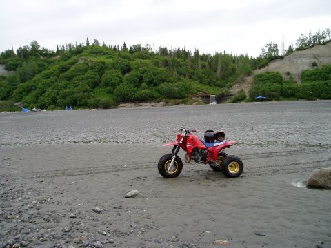 2000 Ford E350 - Three-wheeled ATV sits on a beach with a wooded hillside and a small waterfall.