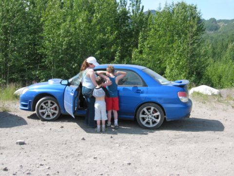 1978 Ford Bronco - A blue Subaru Impreza WRX STI is parked on a dirt road with a family standing around it.