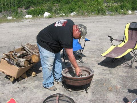 1978 Ford Bronco - A man prepares a fire pit for a gathering, with camping chairs and firewood visible.