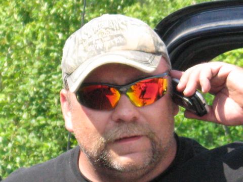 1978 Ford Bronco - A man in sunglasses and a camouflage cap speaks on a flip phone, with the open door of a vehicle visible behind him.