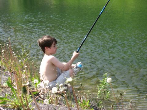 1978 Ford Bronco - A young boy sits on the shore of a lake, casting a fishing line into the water on a sunny day.