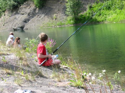 1978 Ford Bronco - A group of children enjoy a day of fishing by the water's edge, with lush green trees and a rocky embankment in the background.