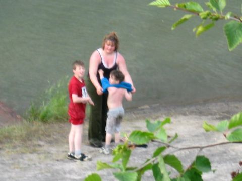 1978 Ford Bronco - A woman helps a child with clothing near the water's edge while another child watches.