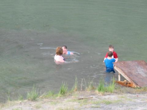 1978 Ford Bronco - Several people are enjoying a swim in a body of water, with a rustic wooden structure visible on the shore.