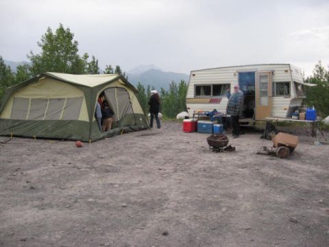 1978 Ford Bronco - A campsite is set up with a large tent and a trailer, camping gear and people enjoying the outdoors.