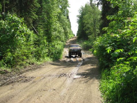 1978 Ford Bronco - A vehicle navigates a challenging, wet dirt road surrounded by dense green forest.