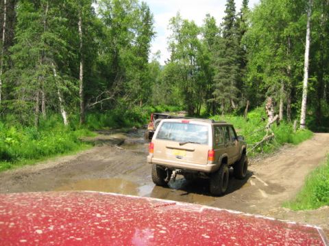 1978 Ford Bronco - Multiple SUVs navigate a muddy trail through a forest.