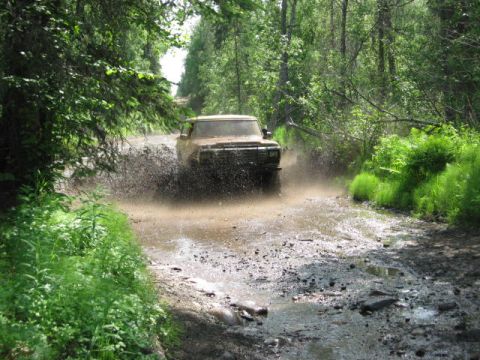 1978 Ford Bronco - A 1978 Ford Bronco kicks up a large spray of mud as it navigates a water-filled trail through a wooded area.
