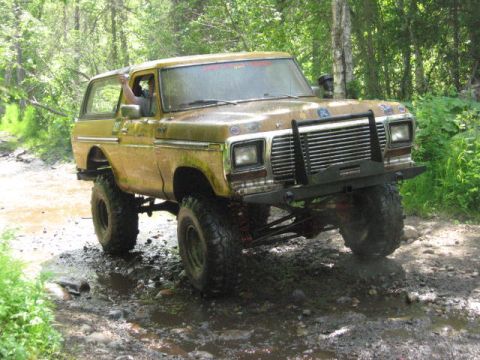 1978 Ford Bronco - Modified 1978 Ford Bronco navigates a muddy trail in a wooded area.