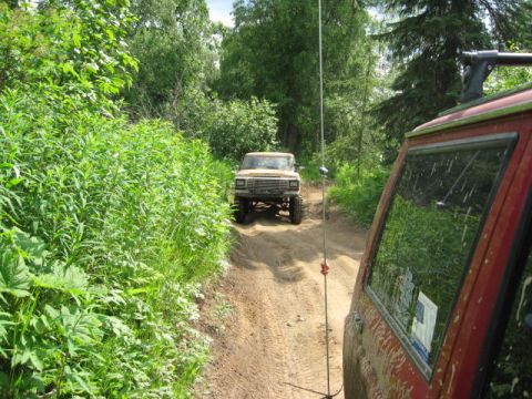 1978 Ford Bronco - A tan 1978 Ford Bronco navigates a wooded dirt road, with another vehicle close behind.
