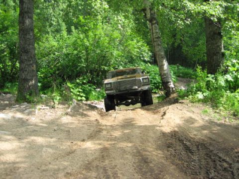 1978 Ford Bronco - A 1978 Ford Bronco navigates a muddy, off-road trail surrounded by lush green trees.