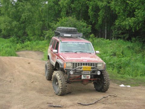 1978 Ford Bronco - A modified red Jeep Cherokee XJ is parked on a dirt path surrounded by greenery.