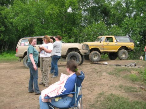 1978 Ford Bronco - A group of people are gathered around SUVs in a wooded area, with a yellow 1978 Ford Bronco prominently featured.