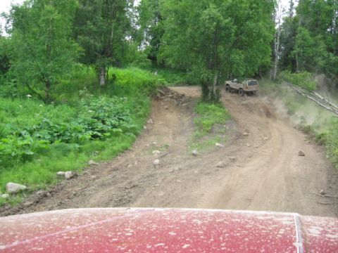 1978 Ford Bronco - A vehicle navigates a dusty, off-road trail surrounded by lush green foliage and trees.