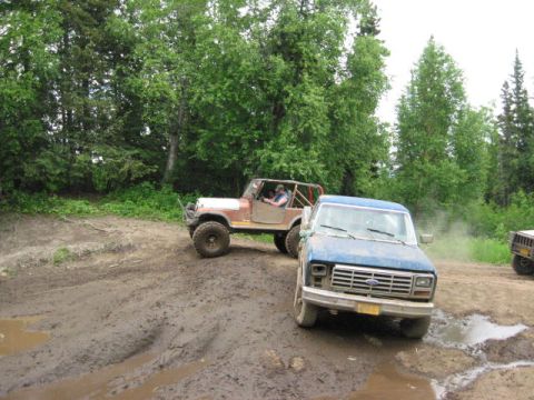 1978 Ford Bronco - A blue Ford pickup truck navigates a muddy trail, followed by a brown Jeep, during an off-road excursion.