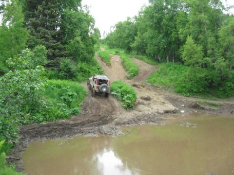 1978 Ford Bronco - An off-road vehicle navigates a challenging muddy terrain with a water obstacle.