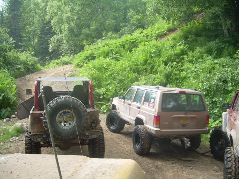1978 Ford Bronco - Multiple off-road vehicles are parked on a dirt path in a wooded area.