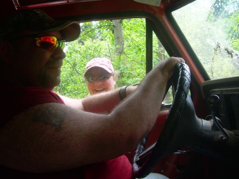 1978 Ford Bronco - Two people inside a vehicle, with trees and foliage seen through the windows.
