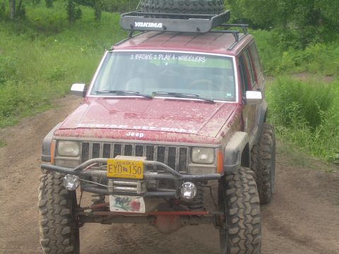 1978 Ford Bronco - Modified Jeep Cherokee XJ with off-road tires and roof rack parked on a dirt path.