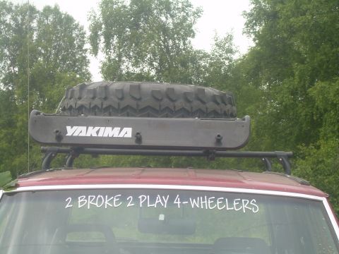 1978 Ford Bronco - A red SUV is equipped with a Yakima roof rack carrying a spare tire, and a humorous decal on the rear window.