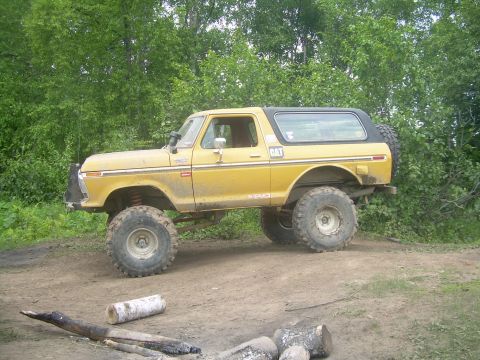 1978 Ford Bronco - This lifted 1978 Ford Bronco, seen in a wooded area, features oversized tires and a black hardtop.