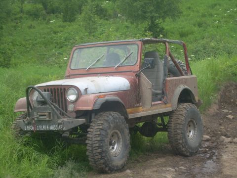 1978 Ford Bronco - A weathered Jeep CJ-7 sits on a muddy trail surrounded by lush green foliage.