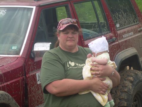 1978 Ford Bronco - A woman holds a baby next to a muddy red Jeep Cherokee.