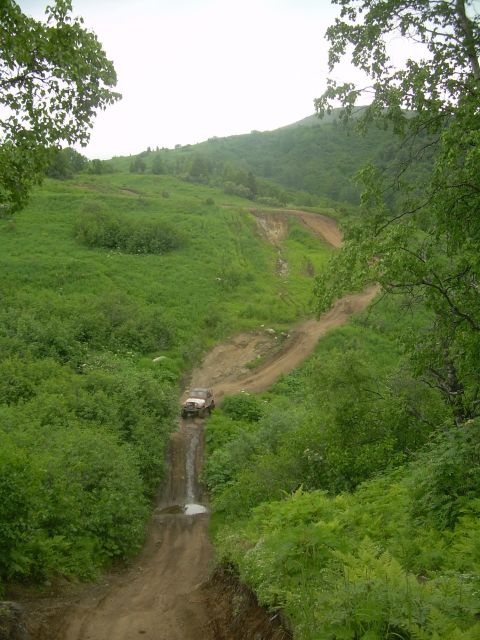1978 Ford Bronco - An off-road vehicle navigates a challenging dirt track through a lush, green landscape.