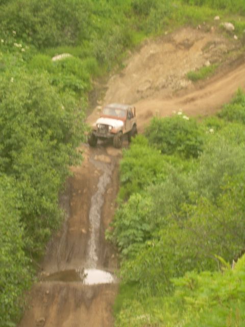 1978 Ford Bronco - A Jeep Wrangler navigates a steep, wet, and muddy off-road trail.