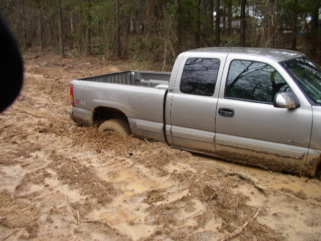 Silver pickup truck stuck in deep mud with trees in the background