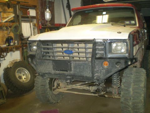 1986 Ford Bronco - Front view of a 1986 Ford Bronco, modified with an aftermarket bumper and grille, parked indoors.
