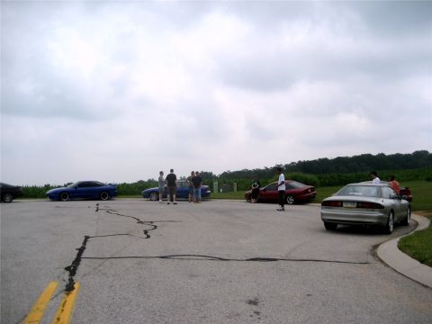 1993 Ford Probe - Cars and people gathered outdoors on a cloudy day. A 1993 Ford Probe is among the vehicles.