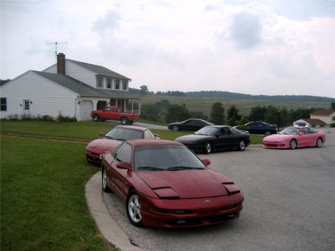 1993 Ford Probe - A collection of Ford Probe sports cars are parked in a driveway and on a street in front of a white house. The cars are various colors incl…