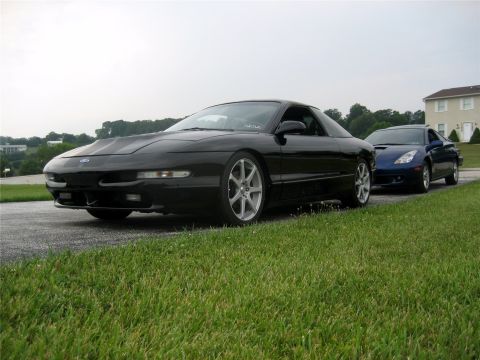 1993 Ford Probe - A black Ford Probe is parked on the side of the road next to a blue Toyota Celica. The Probe is in the foreground, angled towards the viewe…