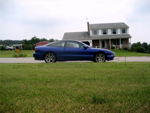 1993 Ford Probe - A blue 1993 Ford Probe is parked on the side of the road in front of a two-story house. The car is viewed from the side, showcasing its cou…