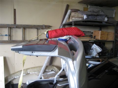 1993 Ford Probe - A silver car bumper and taillight assembly is shown in a cluttered garage setting. A red bag is attached to the assembly by a yellow strap.